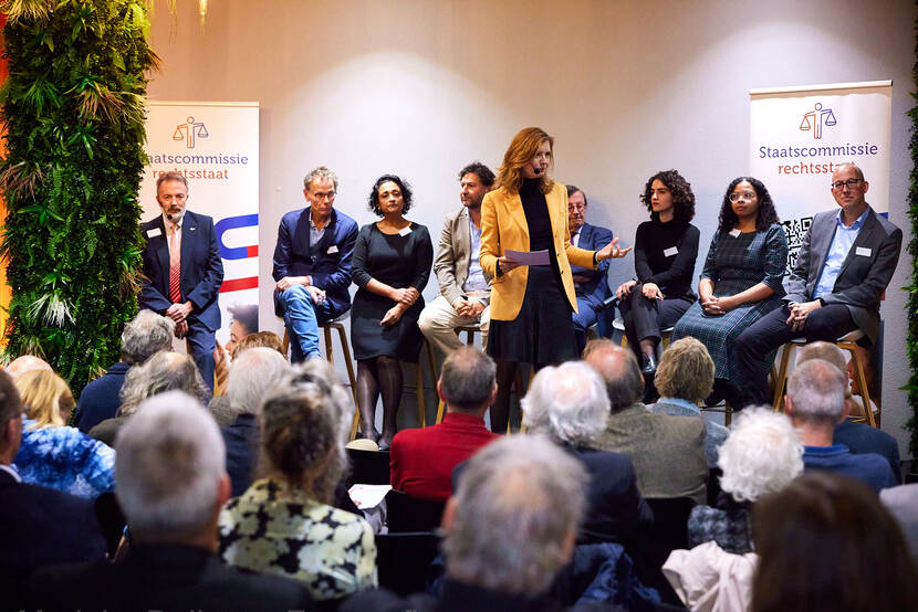 Marcia Luyten aan het woord met de leden van de Staatscommissie rechtsstaat op de achtergrond